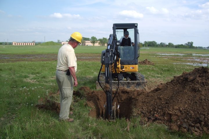 worker observing backhoe excavation