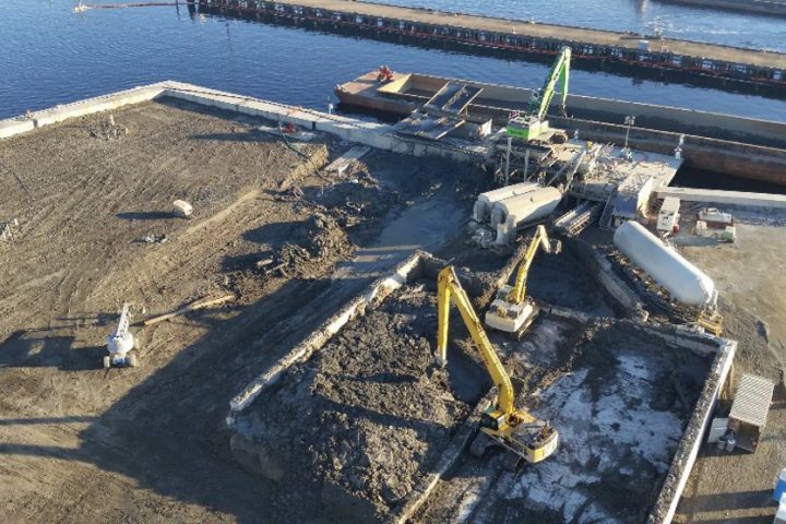 Aerial photo of construction with several excavators moving dirt and a barge in the background.