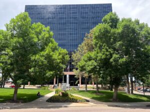 Tall glass office building in Denver with trees and greenspace in front.