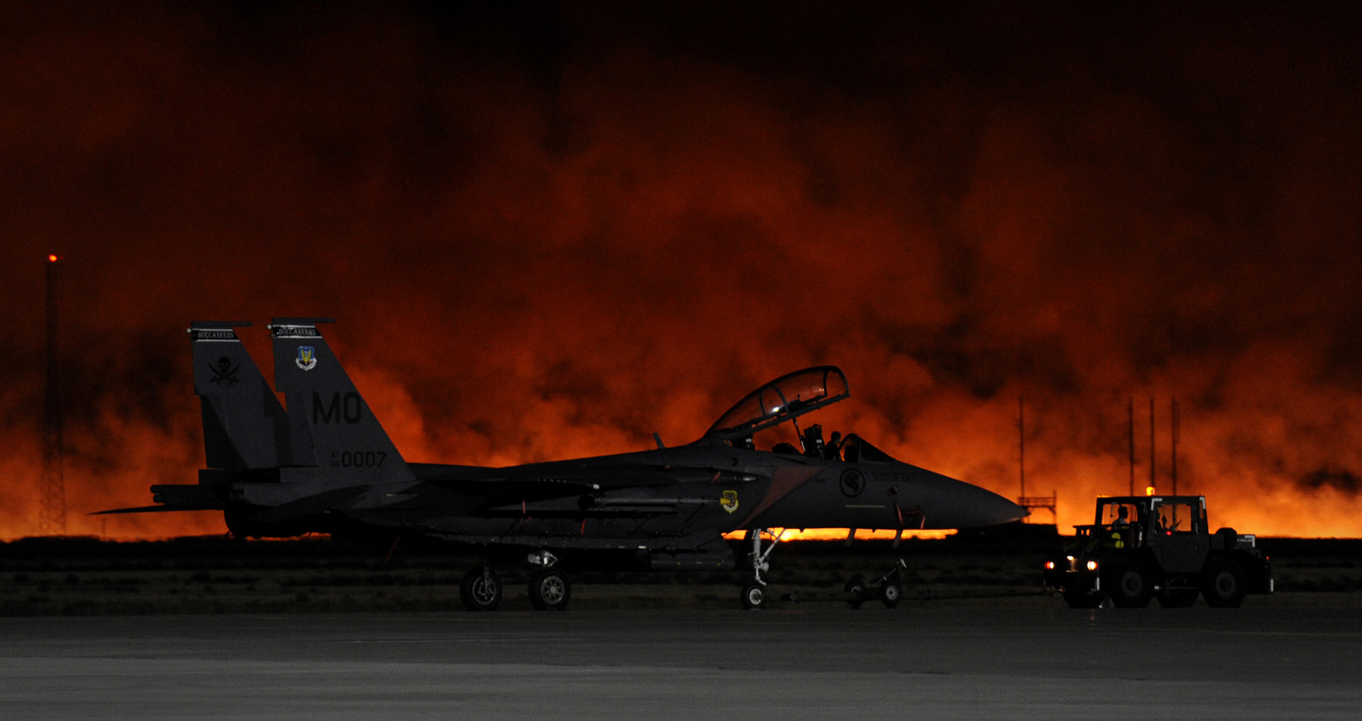 A brush fire from a lightning strike reddens the evening sky behind an F-15SG at Mountain Home Air Force Base, Idaho. 