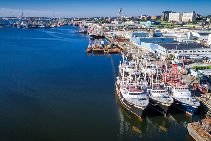 Port of New Bedford Massachusetts with fishing boats in the foreground, and a crane and other vessels in the background – Photo credit to SRPEDD