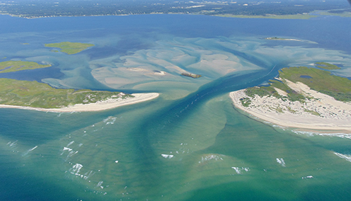 Aerial photo of breach at Fire Island showing channel of dark water through two spits of land.