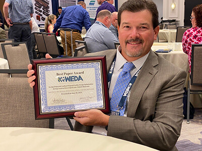 At the WEDA conference, Jamie Beaver holds the just-bestowed Best Paper Award plaque for the design optimization for a dredged material confined disposal facility.