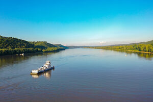 Aerial view of a tugboat navigating the Ohio River between Indiana and Kentucky, gracefully sailing on a river amidst mountainous terrain.