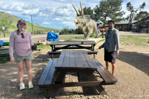 Two EA Denver employees painting a picnic table at Dinosaur Ridge with dinosaur statue in the background.