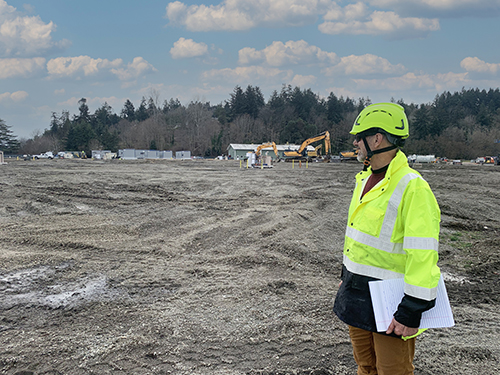 EA Project Manager stands in the foreground while construction activities and equipment is visible in the background
