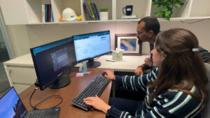 Two engineers at a desk remotely viewing dashboards on two monitors.