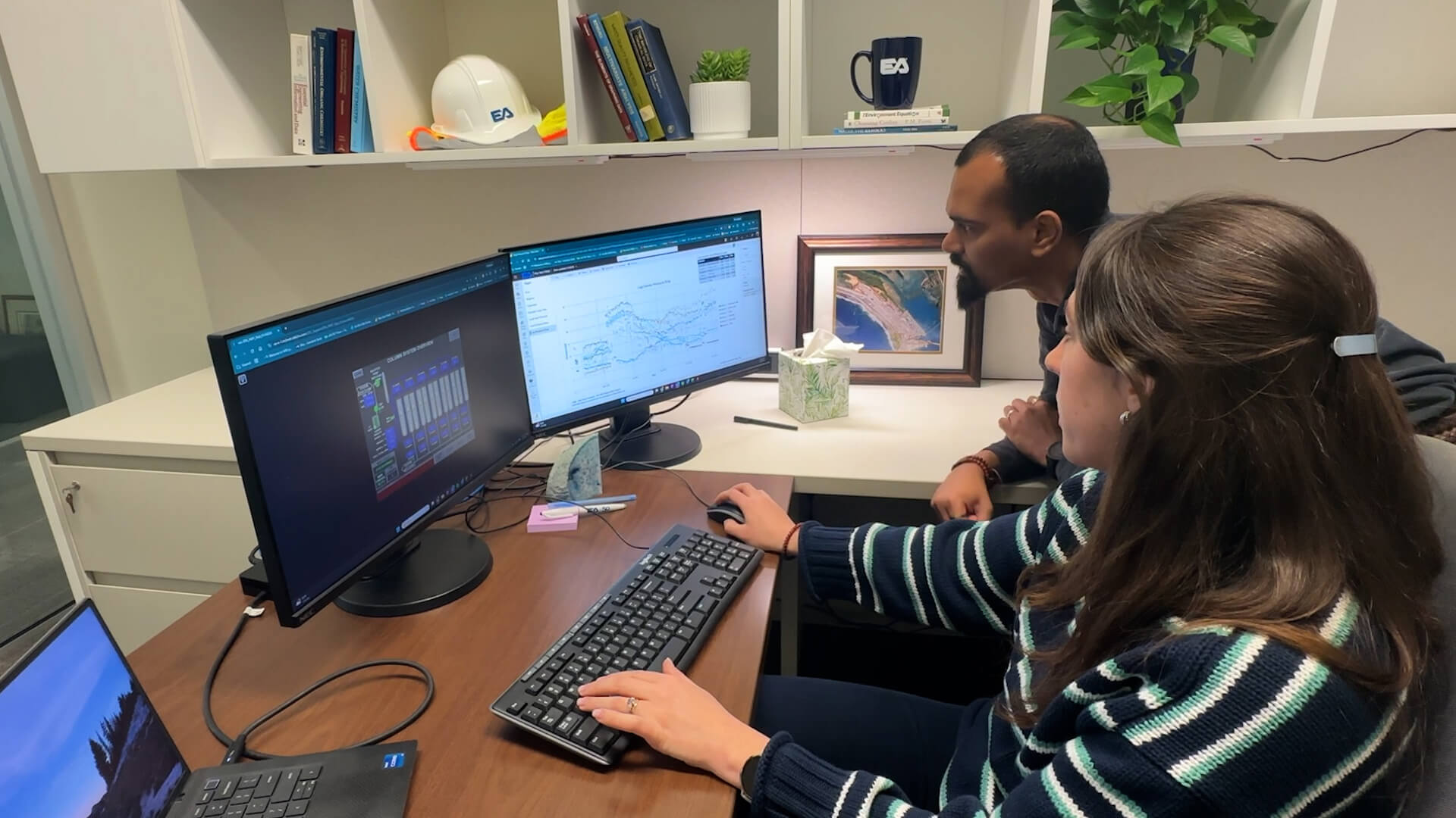 Two engineers at a desk remotely viewing dashboards on two monitors.
