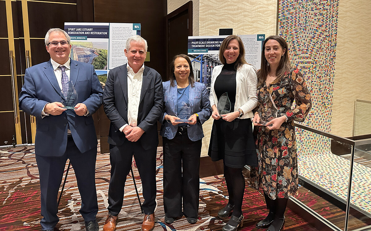 - Mike Ciarlo, Kelly Whalen, Sanita Corum, Jamie Suski, and Ali Peters holding their engineering excellence awards while standing in front of display boards highlighting the Spirit Lake Remediation and Restoration and the Drinking Water PFAS treatment projects.