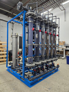 - Pilot system featuring 12 vertical cylinders and complex valves, piping, pumps, and metering prior to installation at a water treatment plant.