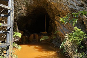 Opening of rock at the Copper Bluff Mine with copper colored water in the foreground and into the shaft.