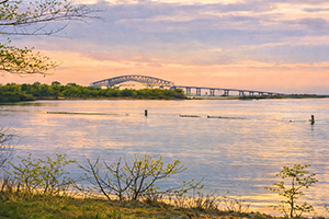 Photograph of open water in Bear Creek at sunset with the old Key Bridge in the background and the shoreline in the foreground